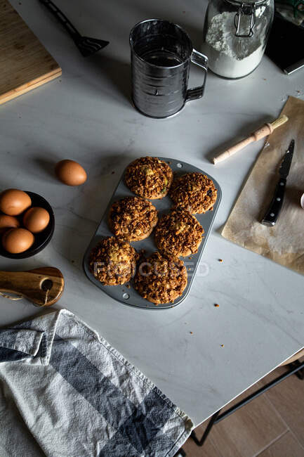 From above composition of delicious cupcakes with walnuts in baking dish eggs peaches flour and parchment paper arranged on white surface — Stock Photo