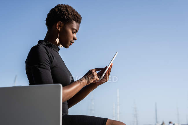 Вид з боку концентрованих афро-американської жінки в елегантному чорному платті за допомогою мобільного телефону — стокове фото