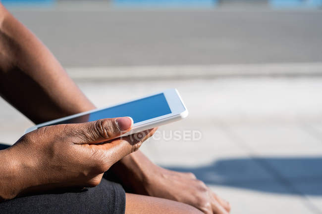Ritagliato di donna nera irriconoscibile utilizzando il telefono cellulare mentre seduto sul marciapiede — Foto stock