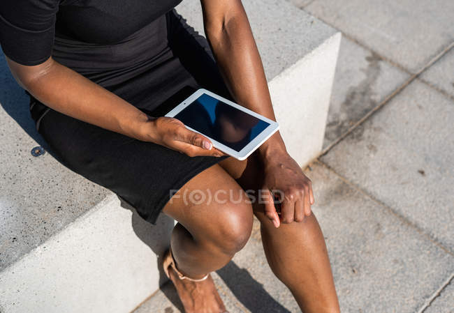 Ritagliato di donna nera irriconoscibile utilizzando il telefono cellulare mentre seduto sul marciapiede — Foto stock