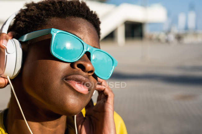 Афроамериканець жінка в стильних яскравих синіх сонцезахисних окулярів за допомогою навушників — стокове фото