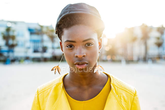 Портрет афро-американської жінки в стильному яскравому піджаку дивлячись у камеру на піщаному пляжі розмитий фон — стокове фото