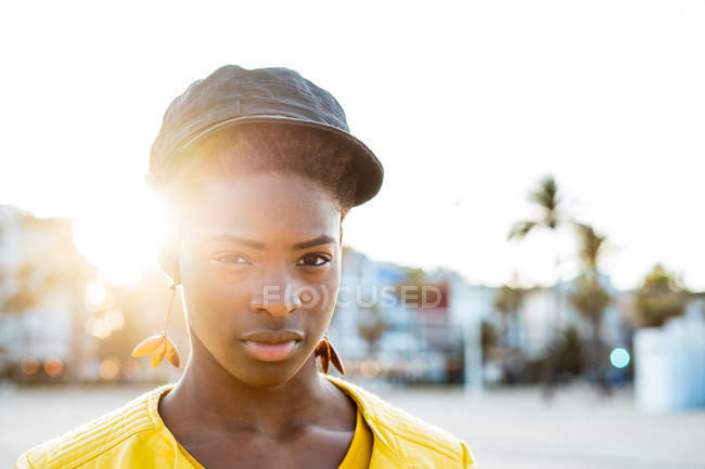 Retrato de mujer afroamericana en chaqueta brillante con estilo mirando en la cámara en la playa de arena fondo borroso - foto de stock