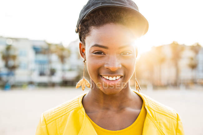Портрет щасливого афро-американської жінки в стильному яскравому піджаку дивлячись у камеру на піщаному пляжі розмитий фон — стокове фото