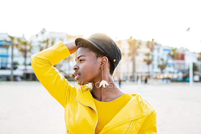 Portrait of African American woman in stylish bright jacket looking away on sandy beach blurred background — Stock Photo