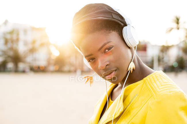 Portrait of African American woman in stylish bright jacket looking in camera on sandy beach blurred background — Stock Photo