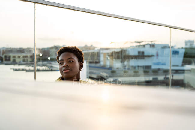 Mise au point sélective vue de côté de la femme afro-américaine sereine se refroidissant sur le balcon en verre et regardant loin — Photo de stock