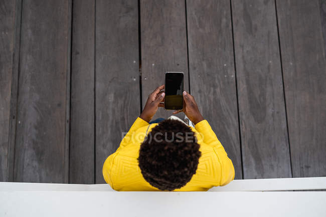 Vista superior de una mujer negra irreconocible apoyada en la pared mientras usa el teléfono móvil - foto de stock