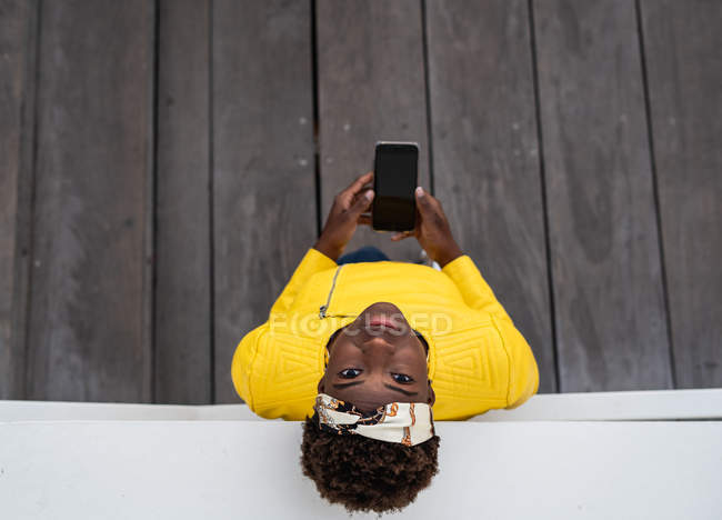 Вид сверху современной афроамериканки, опирающейся на стену современного здания при использовании мобильного телефона — стоковое фото