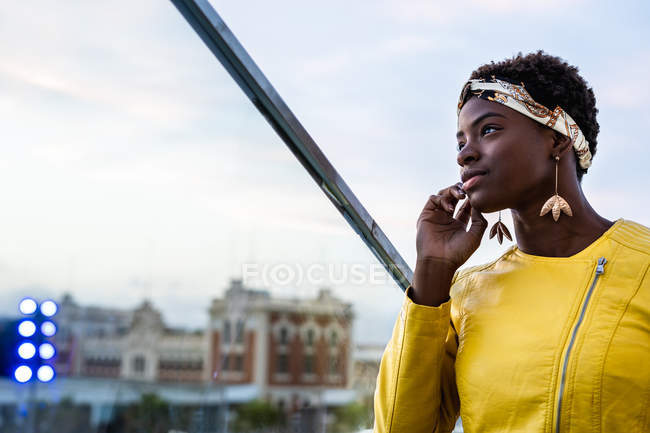 Vue latérale de la femme afro-américaine sereine se refroidissant sur un balcon en verre et regardant loin — Photo de stock