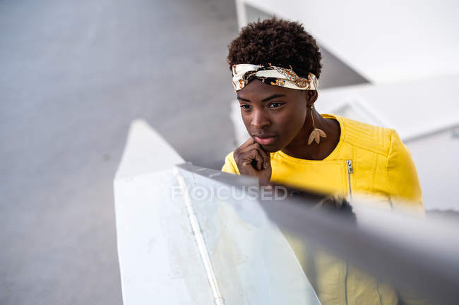 Angle élevé de femme afro-américaine heureuse dans l'usure élégante refroidissant sur les escaliers s'appuyant sur la main courante et détournant les yeux — Photo de stock