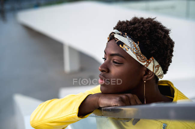 Alto angolo di donna afro-americana felice in elegante usura agghiacciante sulle scale appoggiate sul corrimano e guardando altrove — Foto stock