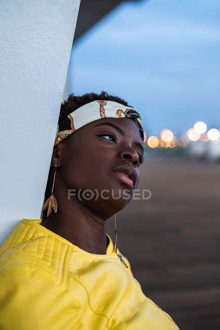 Vista lateral da mulher afro-americana apoiada na parede do edifício moderno e olhando para longe — Fotografia de Stock