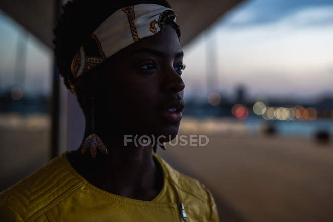Vue latérale de la femme afro-américaine sereine se refroidissant sur un balcon en verre et regardant loin le soir — Photo de stock