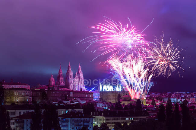 Fuegos artificiales coloridos lejanos junto a las torres de la Catedral de Santiago de Compostela en púrpura tarde astuto - foto de stock