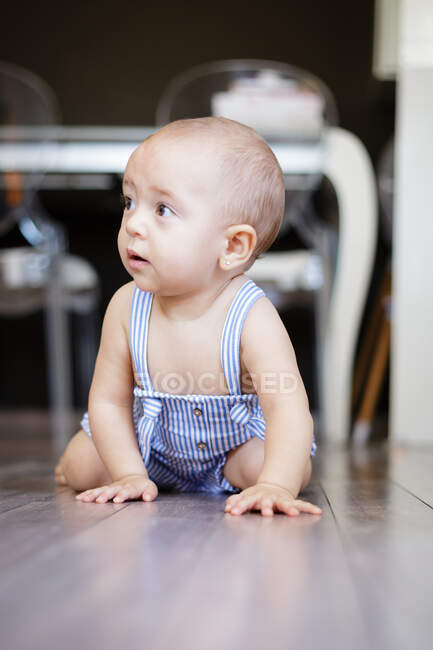 Возбужденный босоногий ребенок смотрит в сторону, сидя на паркете возле прилавков в уютной кухне дома — стоковое фото