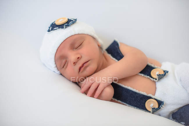 Adorable newborn baby in hat and pants peacefully sleeping on soft white mattress at home — Stock Photo