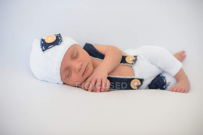 Adorable newborn baby in hat and pants peacefully sleeping on soft white mattress at home — Stock Photo
