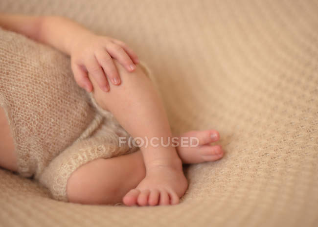 Imagen recortada de bebé descalzo acostado con las piernas cruzadas sobre una sábana blanca y durmiendo en casa - foto de stock