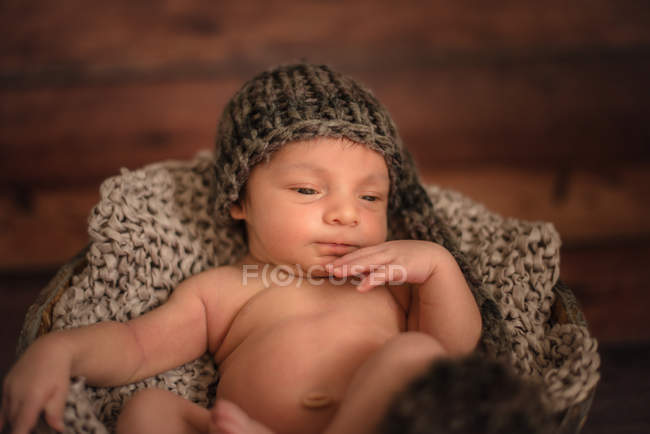 Bebé desnudo en sombrero de punto en cubo en el suelo de madera en casa - foto de stock