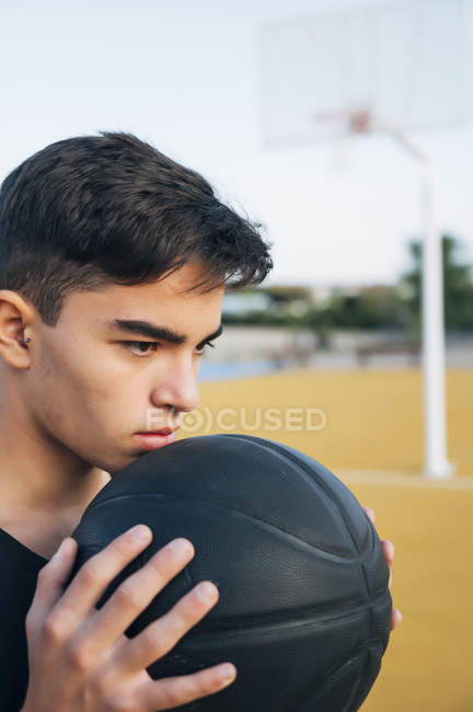 Jovem segurando bola enquanto joga no campo de basquete amarelo ao ar livre . — Fotografia de Stock