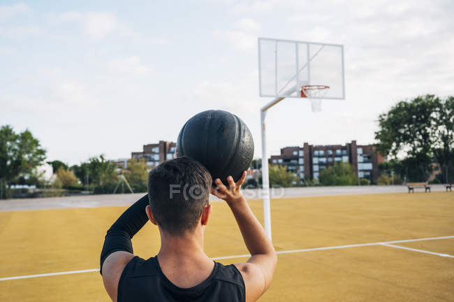 Young man throwing ball while playing on basketball court outdoors in rear view. — Stock Photo