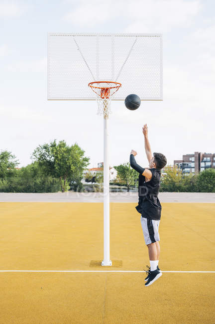 Молодой человек бросает мяч во время игры на баскетбольной площадке . — стоковое фото