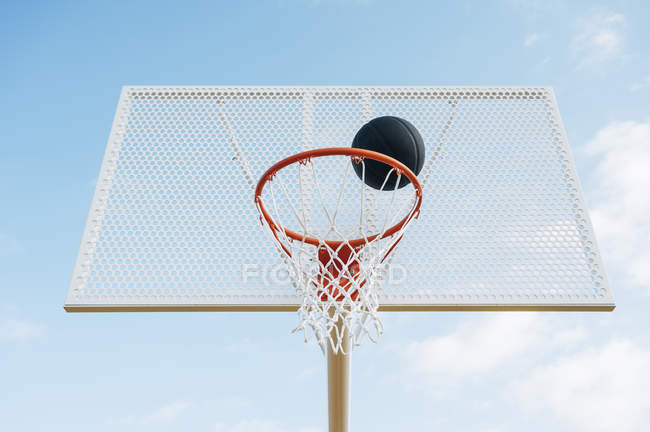 Відкрита баскетбольна сітка і чорний м'яч в суді проти блакитного неба знизу . — стокове фото