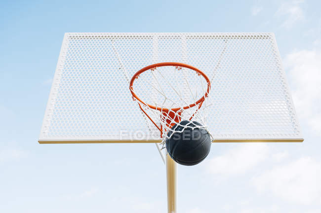 Outdoor basketball black ball in net in court against blue sky from below. — Stock Photo