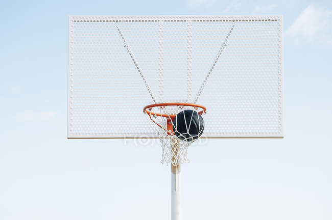 Outdoor basketball black ball in net in court against blue sky. — Stock Photo