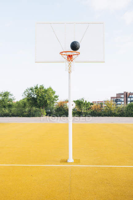 Schwarzer Ball im Netz auf gelbem Basketballfeld. — Stockfoto