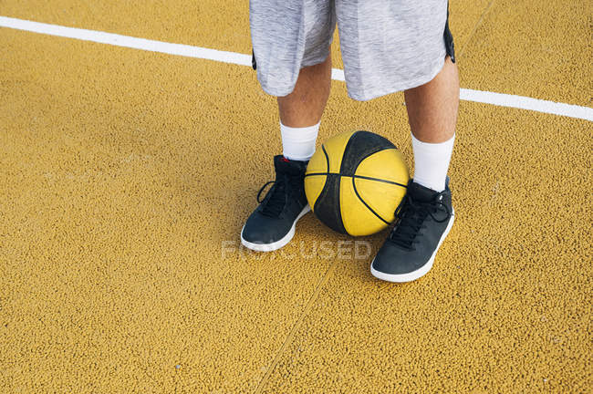 Piernas de joven jugando con pelota en cancha de baloncesto al aire libre . - foto de stock