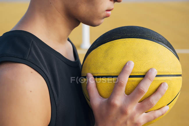 Recortado de hombre joven sosteniendo la pelota mientras juega en la cancha de baloncesto al aire libre . - foto de stock