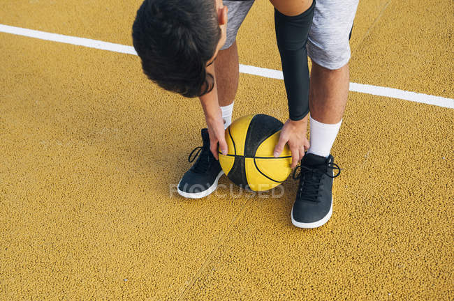 Молодой человек склоняется к мячу во время игры на баскетбольной площадке на открытом воздухе . — стоковое фото