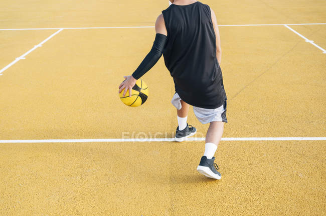 Обрезанный молодой человек, играющий с мячом на баскетбольной площадке на открытом воздухе . — стоковое фото