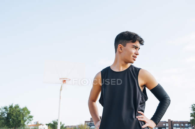 Молодой человек в черном стоит на баскетбольной площадке на улице . — стоковое фото