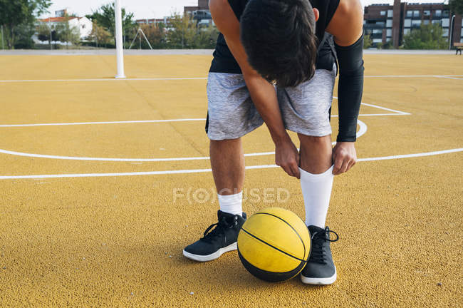 Junger Mann auf Basketballplatz fixiert Socken. — Stockfoto