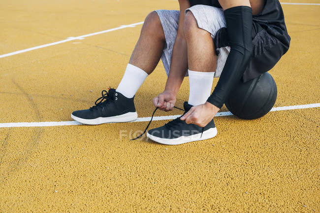 Jovem no campo de basquete corrigindo cadarços . — Fotografia de Stock