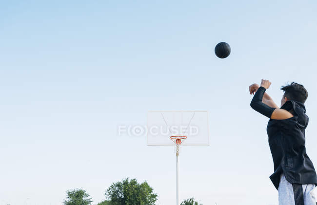 Jovem jogando bola enquanto joga no campo de basquete ao ar livre . — Fotografia de Stock