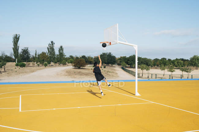 Jovem jogando no campo de basquete amarelo ao ar livre . — Fotografia de Stock