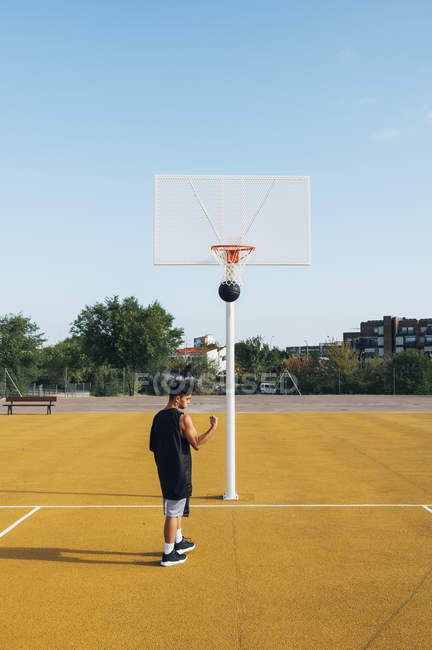 Junger Mann feiert Tor beim Spielen auf gelbem Basketballfeld. — Stockfoto