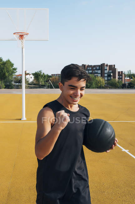 Young man celebrating score while playing on yellow basketball court outdoors. — Stock Photo