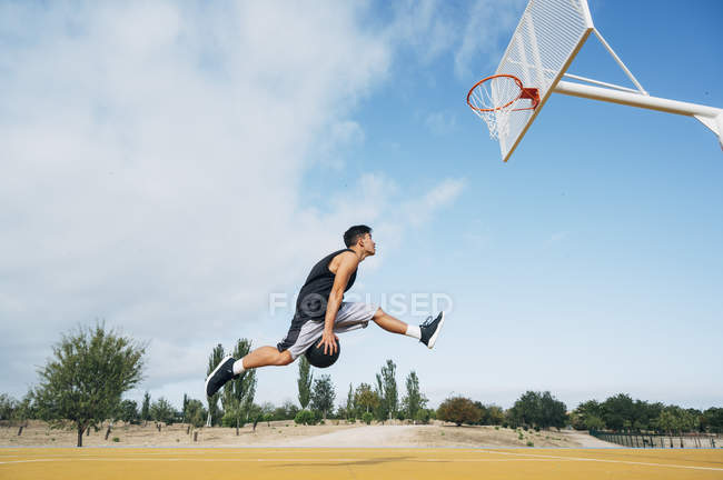 Young man jumping for scoring on basketball court outdoors. — Stock Photo