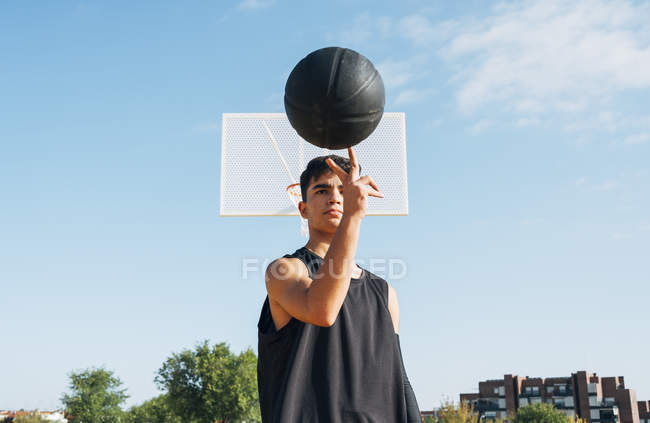Jeune homme posant avec une balle sur le terrain de basket à l'extérieur . — Photo de stock