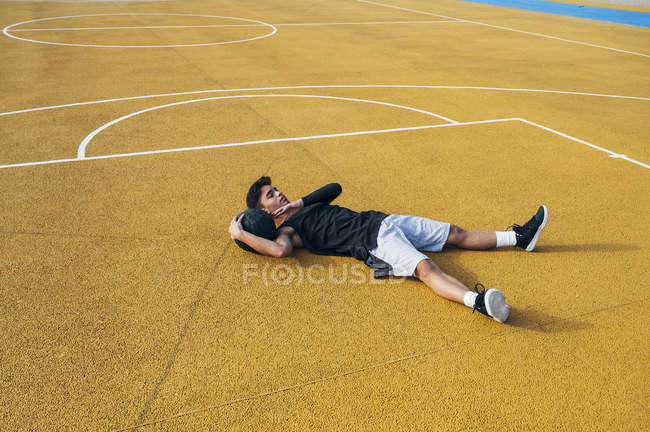 Jovem homem e bola deitado na quadra de basquete ao ar livre descansando depois de jogar basquete . — Fotografia de Stock