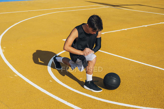 Young man and ball stretching on basketball court outdoors. — Stock Photo