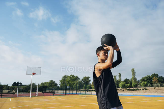Jeune homme jetant la balle tout en jouant sur le terrain de basket en plein air . — Photo de stock