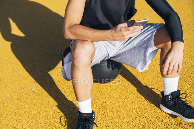 Recadré de joueur de basket-ball masculin en utilisant un smartphone se reposant après la session d'entraînement . — Photo de stock