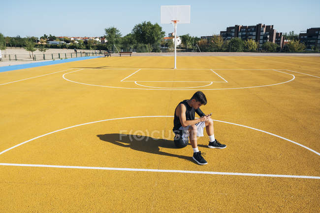 Male basketball player using smartphone resting after training session. — Stock Photo