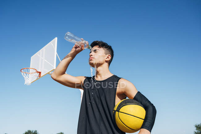 Joven en cancha de baloncesto vertiendo agua de la botella en la cara . - foto de stock